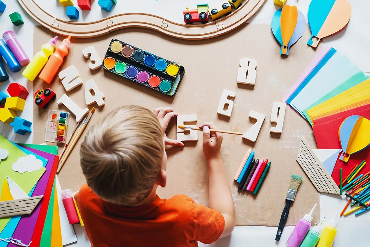A child working with numbers, paints and craft materials on a table